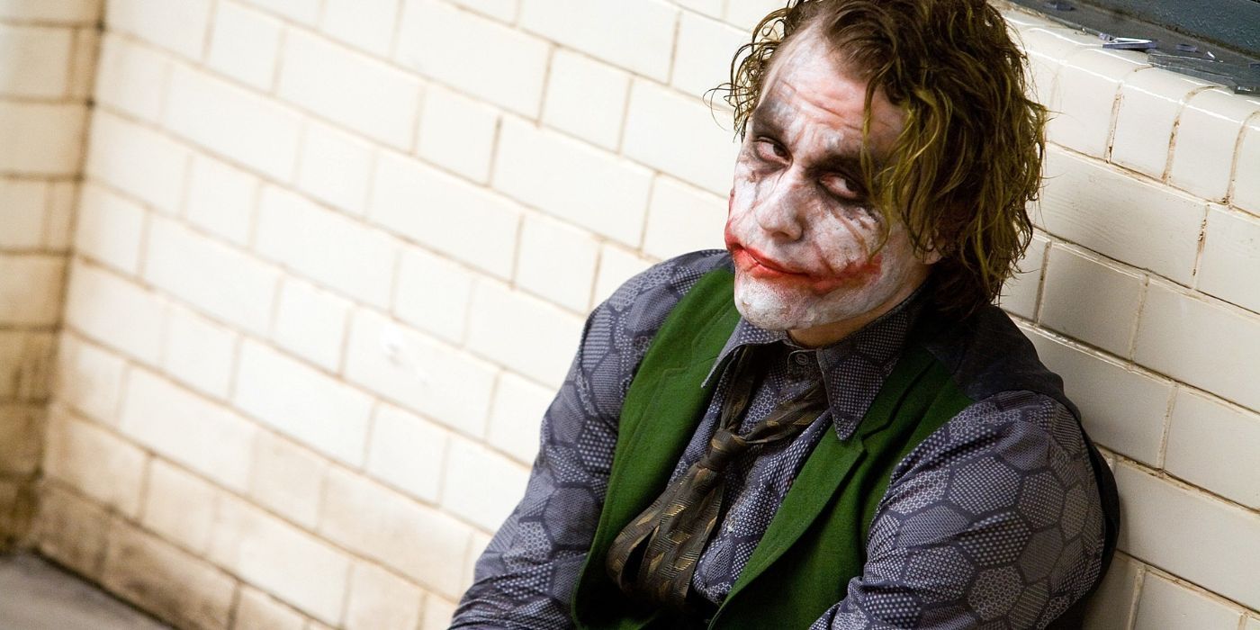 Le Joker (Heath Ledger) est assis sur le sol d'une salle d'interrogatoire, le dos contre le mur dans The Dark Knight